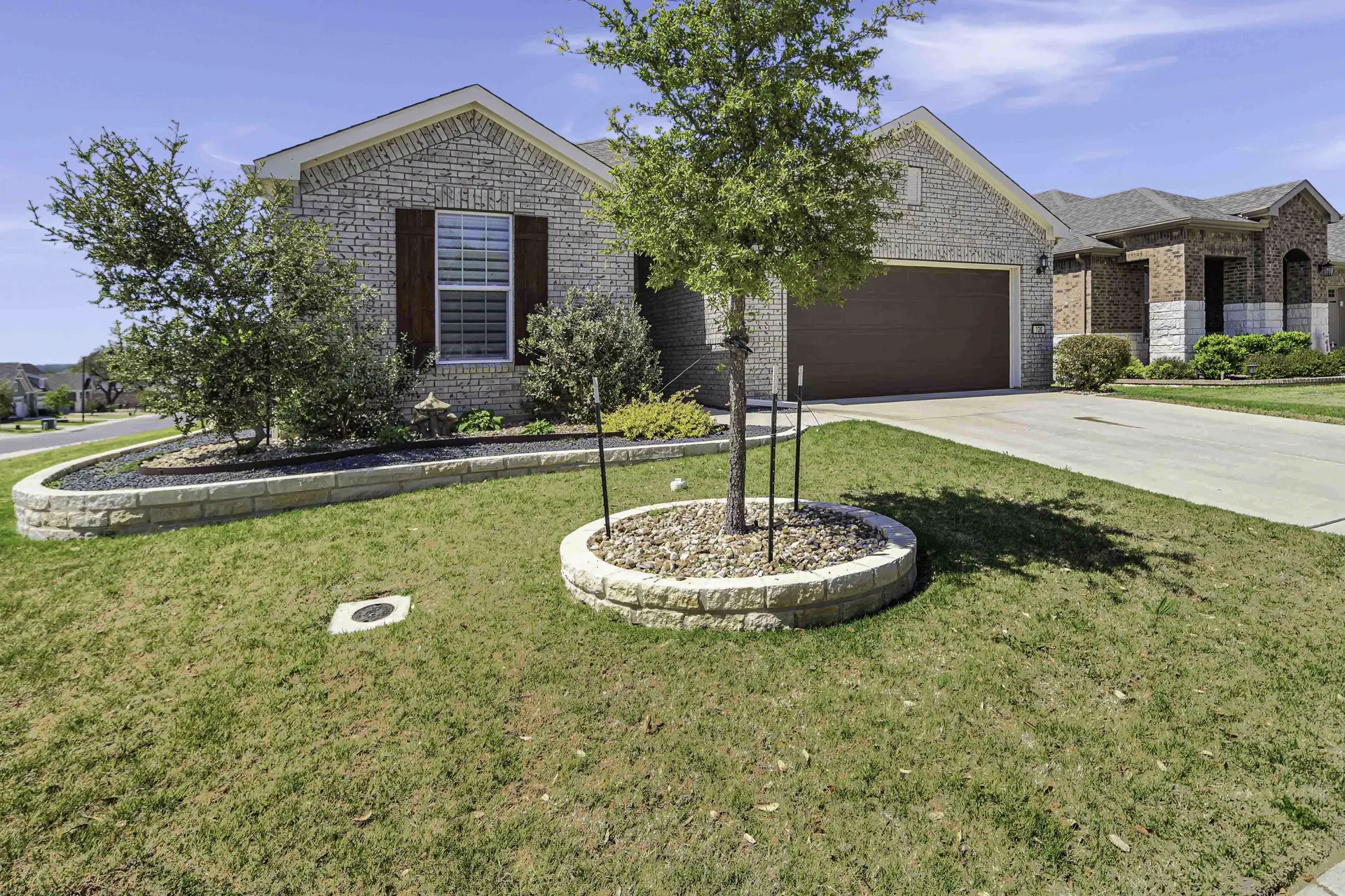 Front yard with landscaped bed, young tree and stone exterior